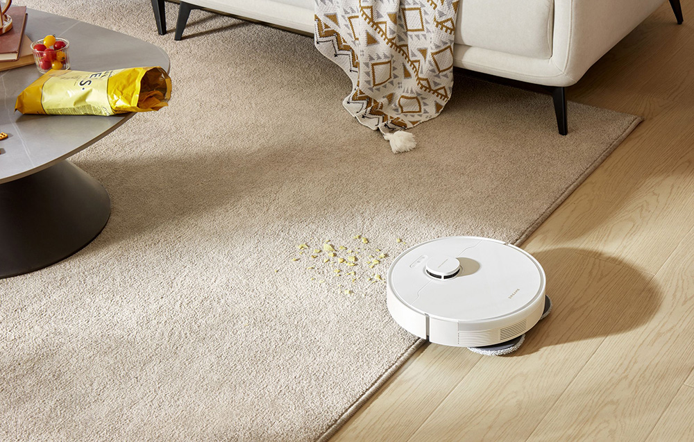 biały robot sprzątający czyści wjeżdża na dywan